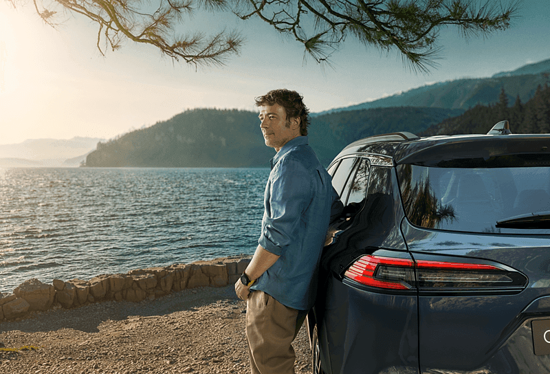 Toyota Center Göteborg Hyrbilar Man lutandes mot en Toyota bil med utsikt över havet och bergen.